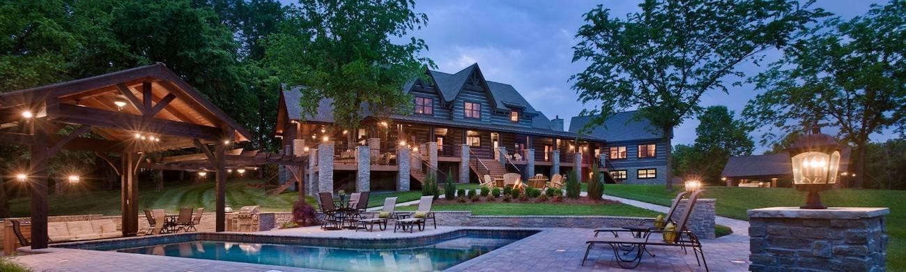 Photo from pool and cabana take of the rear of an estate home with long exterior veranda and three upper dormers and adjacent guest house and garage